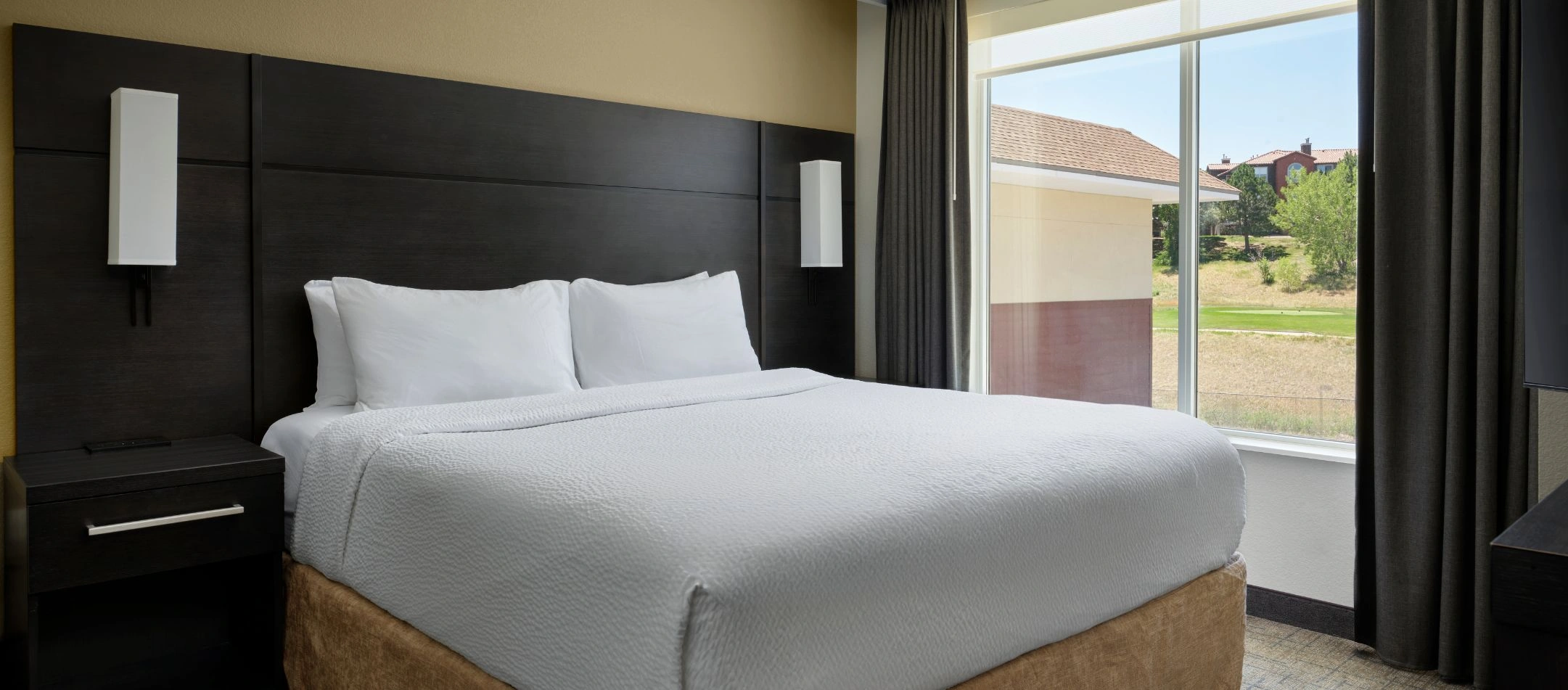 A bedroom with a dark wood headboard and window view at a Broomfield, CO hotel