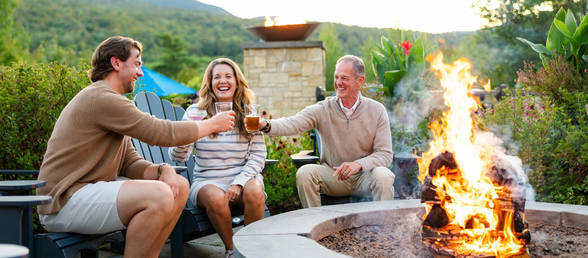 Three hotel guests laughing around a fire pit